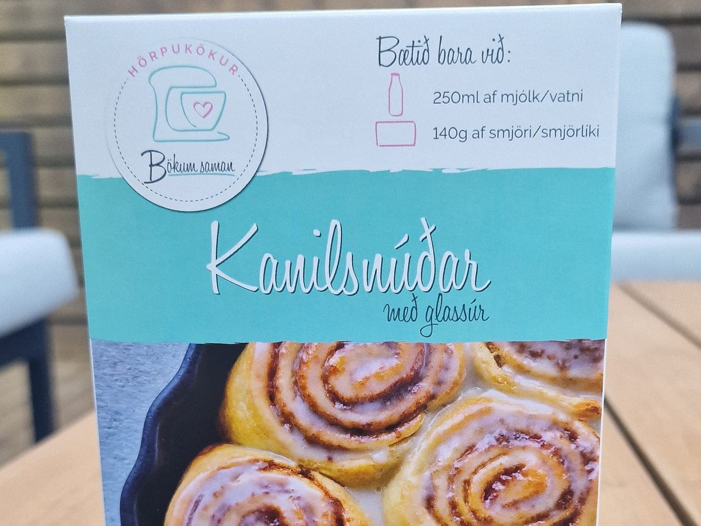 Kanilsnúðakassinn á borði, merki Bökum saman efst til vinstri